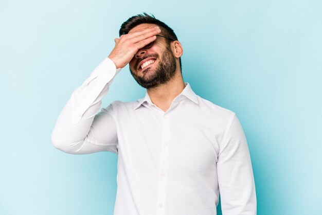 Young caucasian man isolated on blue background laughs joyfully keeping hands on head Happiness concept