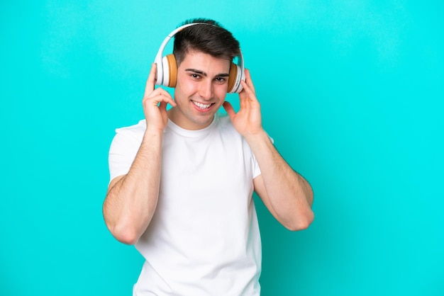 Young caucasian man isolated on blue background listening music