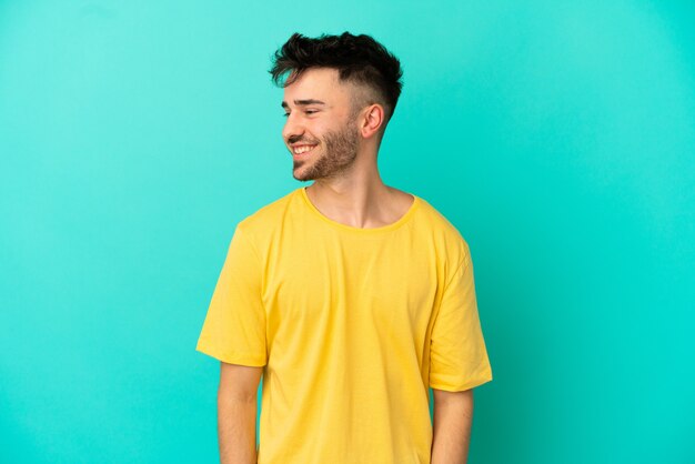 Young caucasian man isolated on blue background looking to the side and smiling