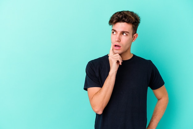 Young caucasian man isolated on blue background looking sideways with doubtful and skeptical expression.