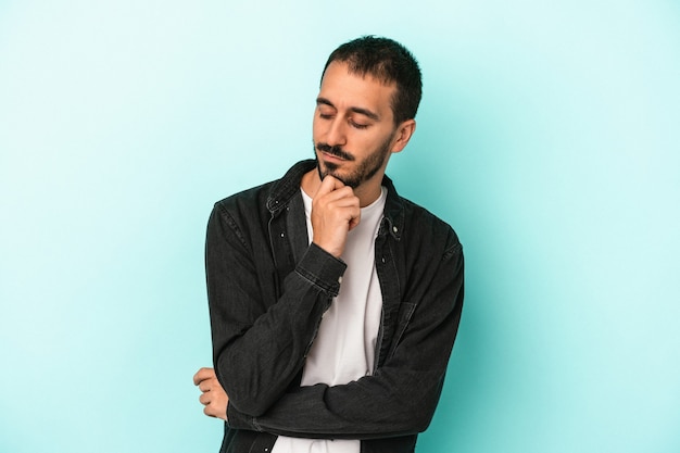 Young caucasian man isolated on blue background looking sideways with doubtful and skeptical expression.