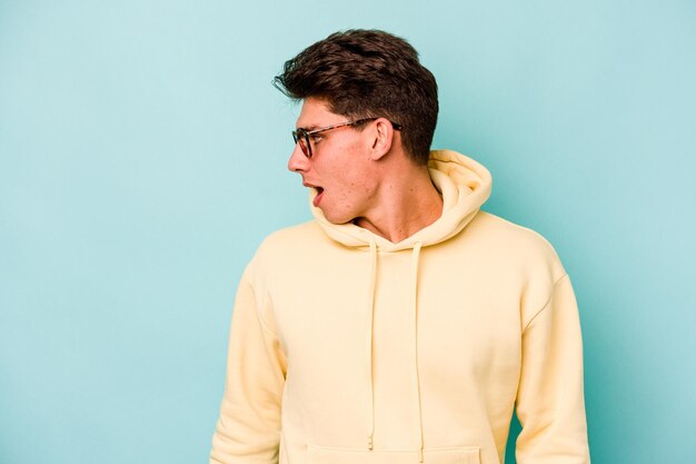 Young caucasian man isolated on blue background looks aside smiling cheerful and pleasant