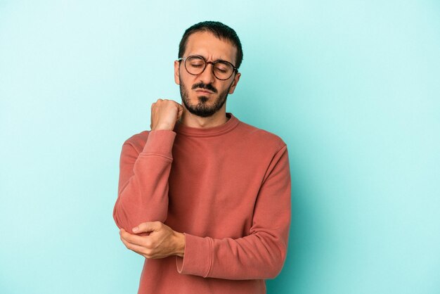 Young caucasian man isolated on blue background massaging elbow suffering after a bad movement