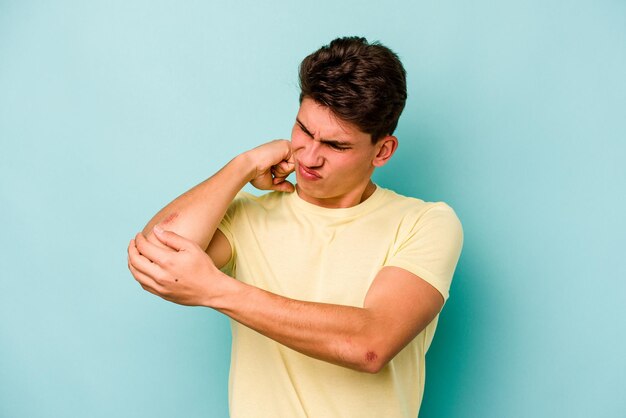 Young caucasian man isolated on blue background massaging elbow suffering after a bad movement