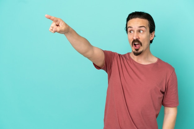 Young caucasian man isolated on blue background pointing away