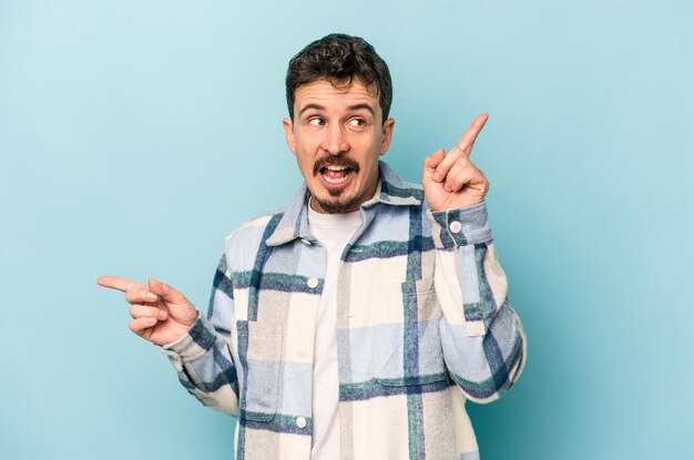 Young caucasian man isolated on blue background pointing to different copy spaces, choosing one of them, showing with finger.