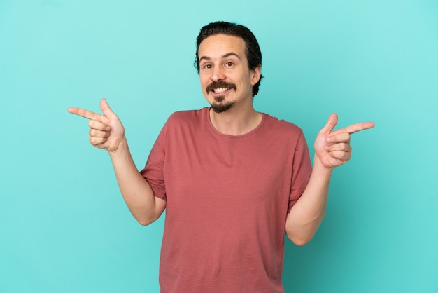 Young caucasian man isolated on blue background pointing finger to the laterals and happy