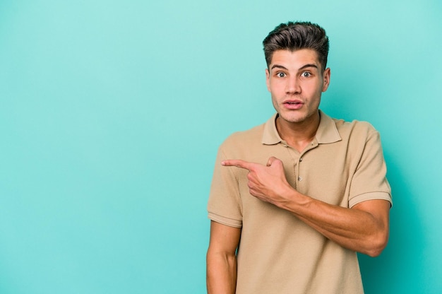 Young caucasian man isolated on blue background pointing to the side