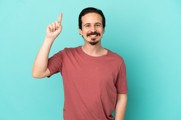 Young caucasian man isolated on blue background pointing up a great idea