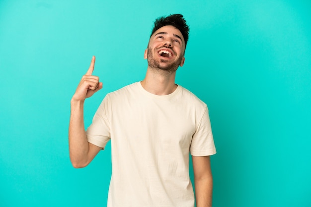 Young caucasian man isolated on blue background pointing up and surprised