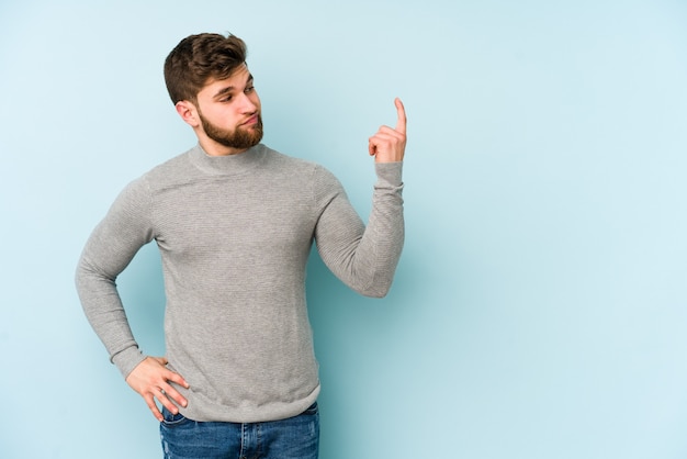 Young caucasian man isolated on blue background pointing with finger at you as if inviting come closer.