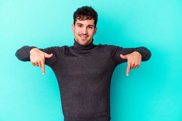 Young caucasian man isolated on blue background points down with fingers, positive feeling.