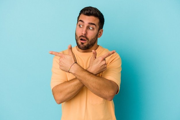 Young caucasian man isolated on blue background points sideways, is trying to choose between two options.