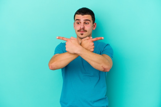 Young caucasian man isolated on blue background points sideways, is trying to choose between two options.