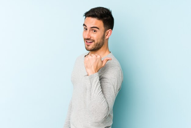 Young caucasian man isolated on blue background points with thumb finger away, laughing and carefree.