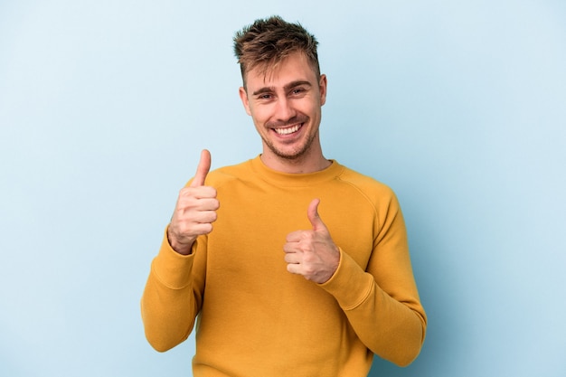 Young caucasian man isolated on blue background raising both thumbs up, smiling and confident.