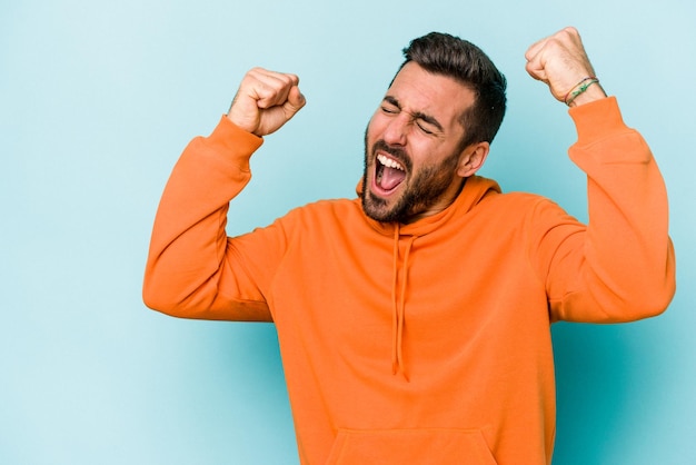 Young caucasian man isolated on blue background raising fist after a victory winner concept