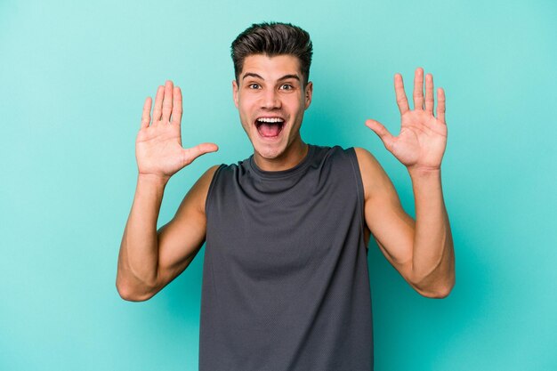 Young caucasian man isolated on blue background receiving a pleasant surprise, excited and raising hands.