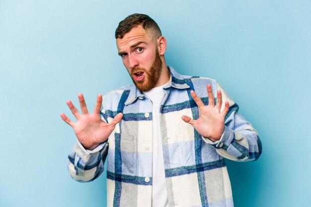 Young caucasian man isolated on blue background rejecting someone showing a gesture of disgust.