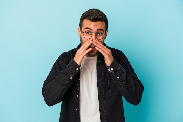 Young caucasian man isolated on blue background saying a gossip, pointing to side reporting something.