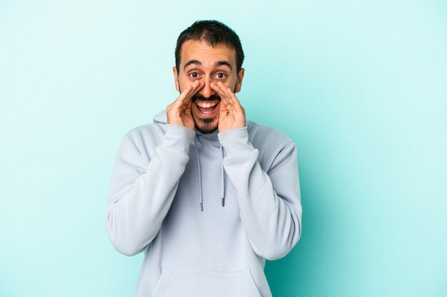 Young caucasian man isolated on blue background saying a gossip, pointing to side reporting something.