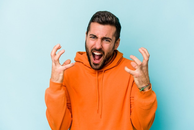 Young caucasian man isolated on blue background screaming with rage