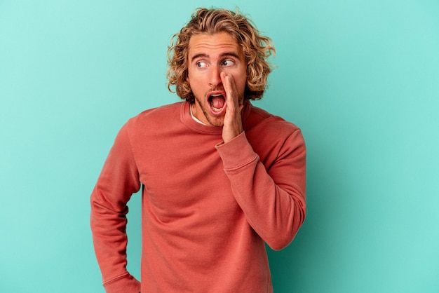 Young caucasian man isolated on blue background shouting excited to front.