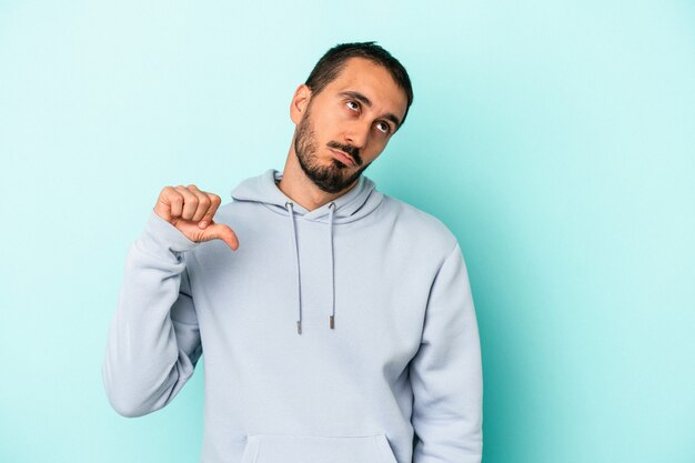 Young caucasian man isolated on blue background showing a dislike gesture, thumbs down. Disagreement concept.