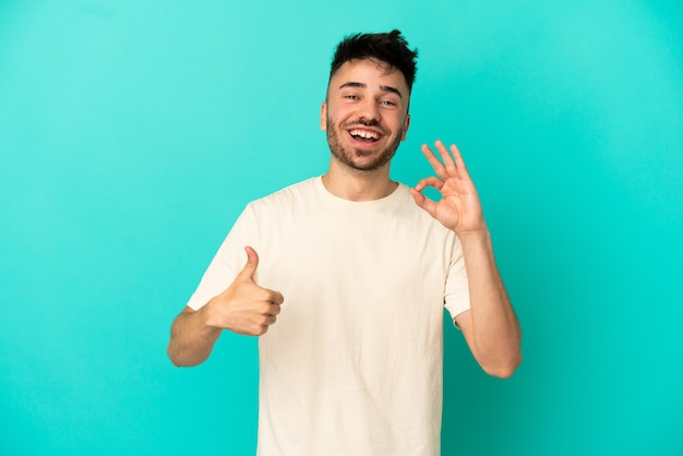 Young caucasian man isolated on blue background showing ok sign and thumb up gesture