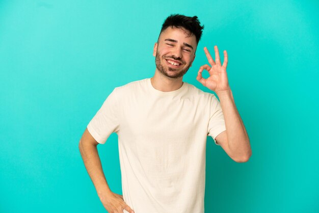 Young caucasian man isolated on blue background showing ok sign with fingers