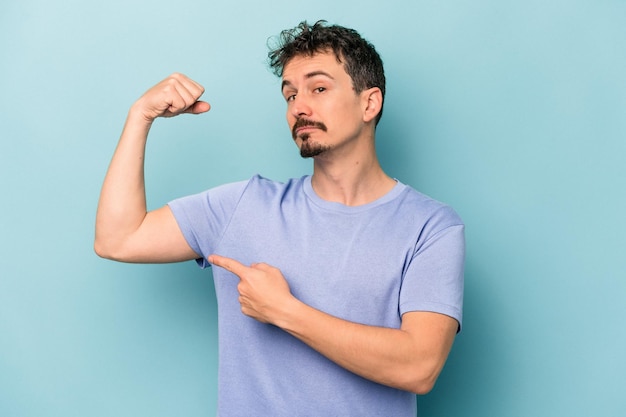 Young caucasian man isolated on blue background showing strength gesture with arms, symbol of feminine power