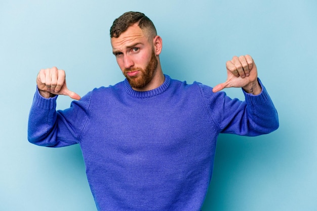 Young caucasian man isolated on blue background showing thumb down, disappointment concept.