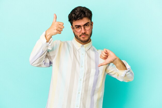 Young caucasian man isolated on blue background showing thumbs up and thumbs down, difficult choose concept