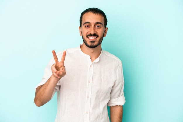 Young caucasian man isolated on blue background showing victory sign and smiling broadly