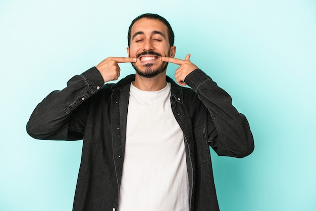 Young caucasian man isolated on blue background smiles, pointing fingers at mouth.