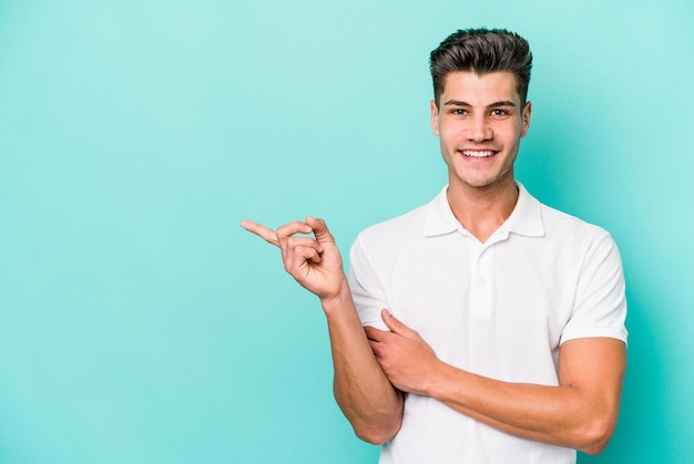 Young caucasian man isolated on blue background smiling cheerfully pointing with forefinger away.