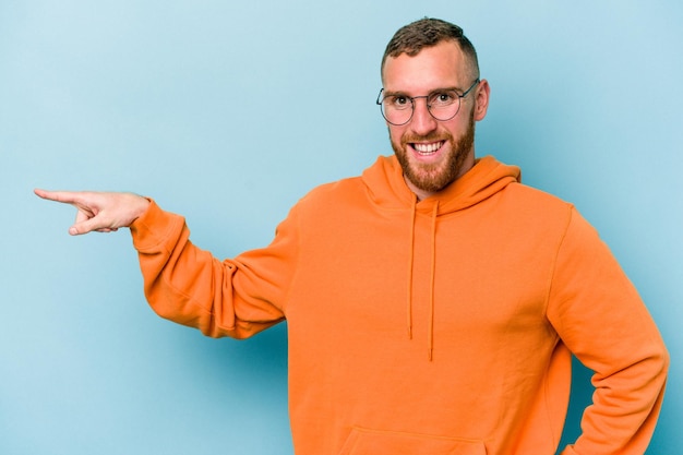 Young caucasian man isolated on blue background smiling cheerfully pointing with forefinger away