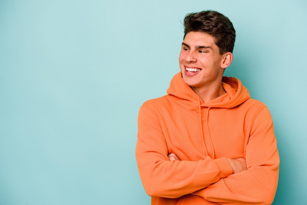 Young caucasian man isolated on blue background smiling confident with crossed arms