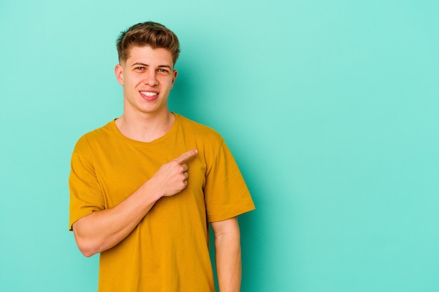 Young caucasian man isolated on blue background smiling and pointing aside, showing something at blank space.