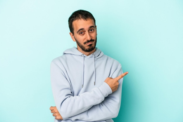 Young caucasian man isolated on blue background smiling and pointing aside showing something at blank space