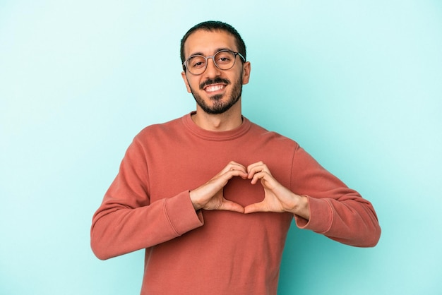 Young caucasian man isolated on blue background smiling and showing a heart shape with hands.