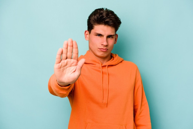 Young caucasian man isolated on blue background standing with outstretched hand showing stop sign preventing you