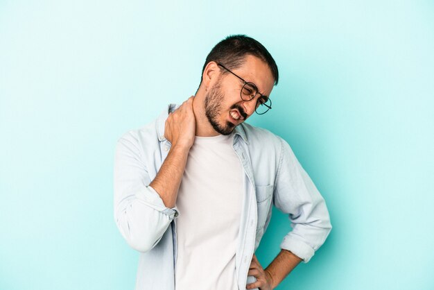 座りがちな生活のために首の痛みに苦しんでいる青い背景で隔離の若い白人男性。