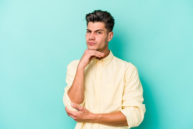 Young caucasian man isolated on blue background suspicious uncertain examining you