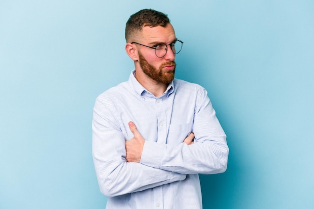 Young caucasian man isolated on blue background suspicious uncertain examining you