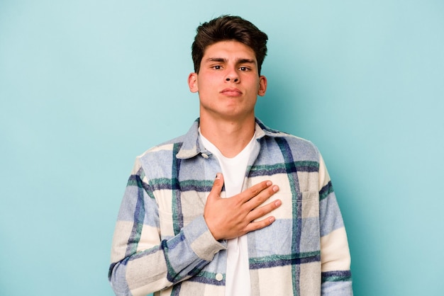 Young caucasian man isolated on blue background taking an oath putting hand on chest