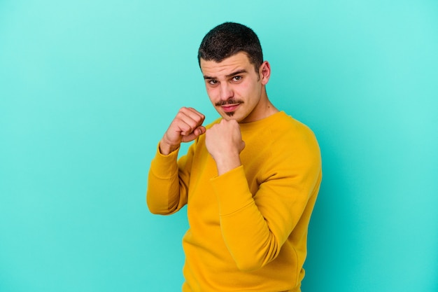 Giovane uomo caucasico isolato su sfondo blu, lanciare un pugno, rabbia, combattimenti a causa di un argomento, boxe.