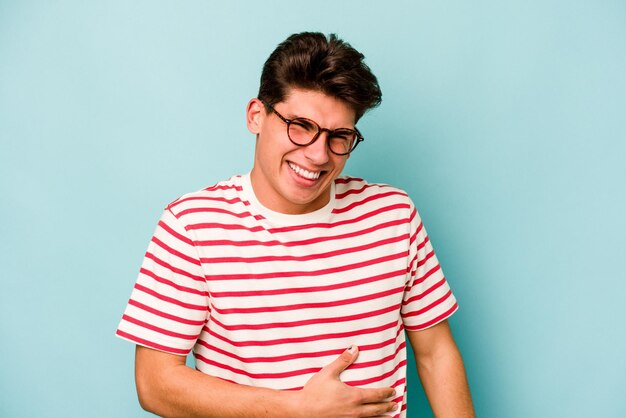 Young caucasian man isolated on blue background touches tummy smiles gently eating and satisfaction concept