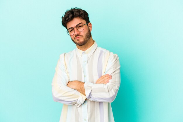 Foto giovane uomo caucasico isolato su sfondo blu infelice guardando a porte chiuse con espressione sarcastica.