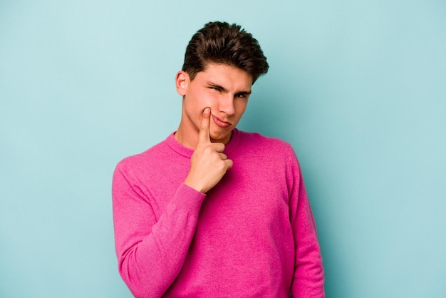 Young caucasian man isolated on blue background unhappy looking in camera with sarcastic expression